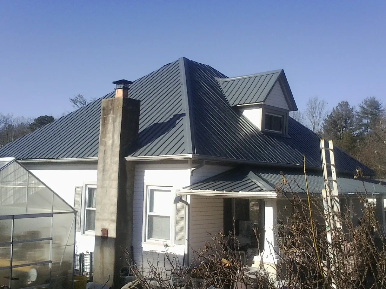 Dark blue standing seam metal roof on a white farmhouse with dormer — Slate & Tile Roof Repair by Roofing Brothers in Westphalia