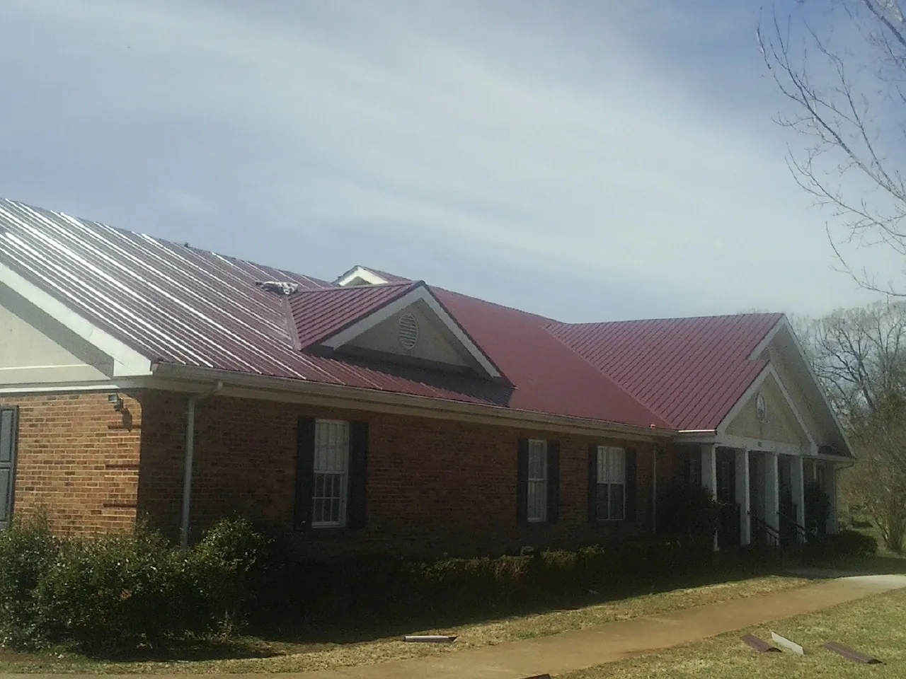 Red metal roof with gabled entries on a long brick building, from a Hail Damage Roof Repair job in Westphalia