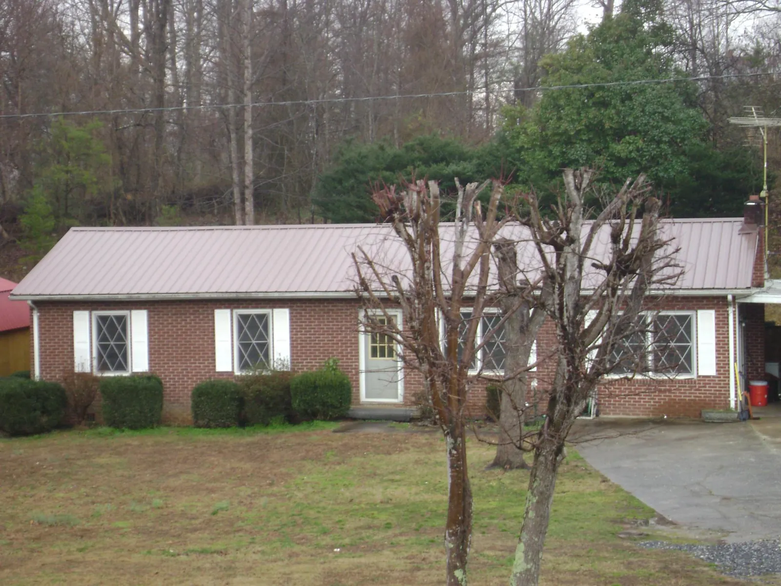 Mauve metal roof on a brick ranch home behind bare trees in Westphalia
